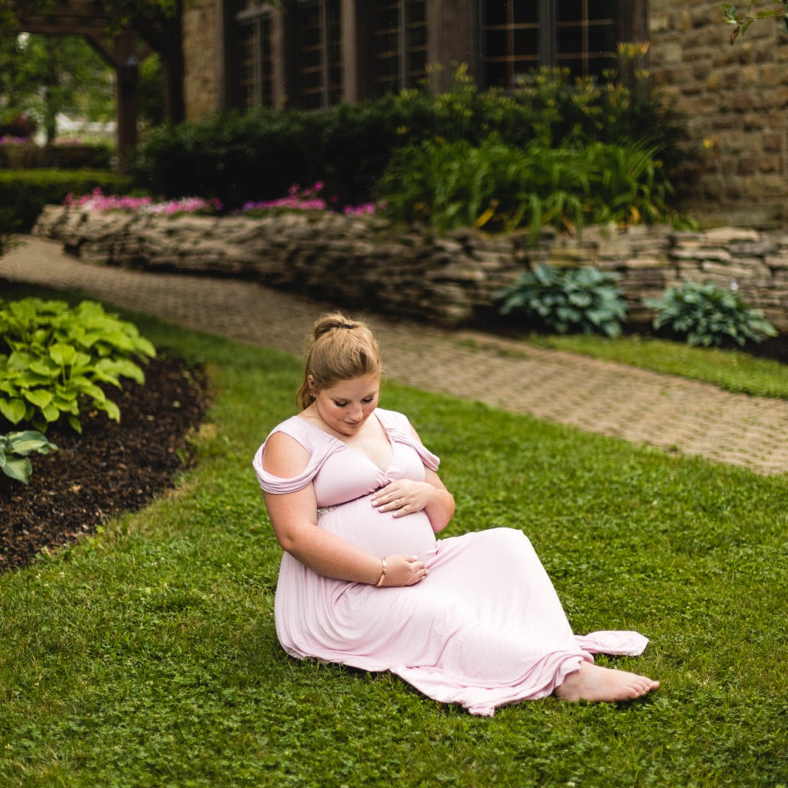 Pregnant mom in pink gown sitting on the grass